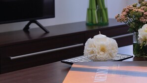 A modern living room with a flat-screen TV, a vase with flowers, and a magazine on a wooden table.
