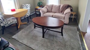 Una sala de estar con un sofá color beige, una mesa de centro de madera, un sillón estampado y una mesita auxiliar con una planta.