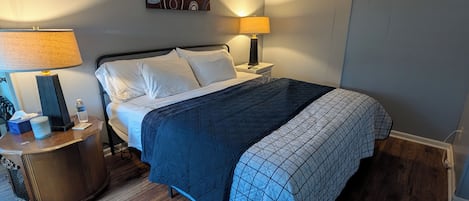 A hotel room with a bed, two bedside tables, a lamp, a wall clock, and a painting.
