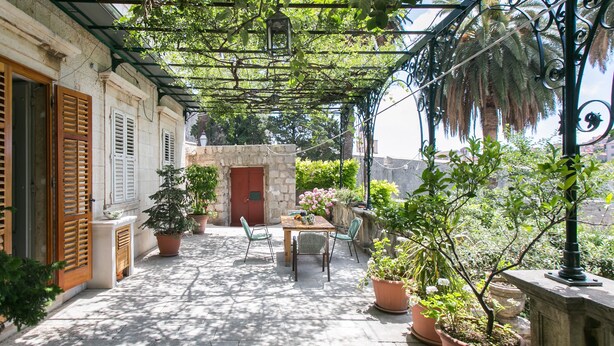 A covered patio with a table and chairs, surrounded by potted plants and a stone wall. - Rooms Posat - Triple Room with Sea View (Dubrovnik)