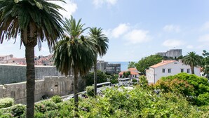 A coastal cityscape with historic buildings, palm trees, and a view of the sea. - Rooms Posat - Triple Room with Sea View (Dubrovnik)