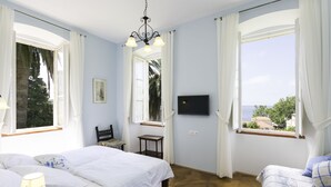 A bedroom with two beds, a TV, and large windows with curtains. - Rooms Posat - Triple Room with Sea View (Dubrovnik)