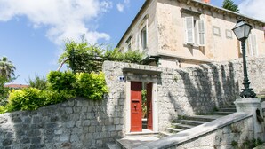 A stone building with a red door and a staircase leading up to it. - Rooms Posat - Triple Room with Sea View (Dubrovnik)