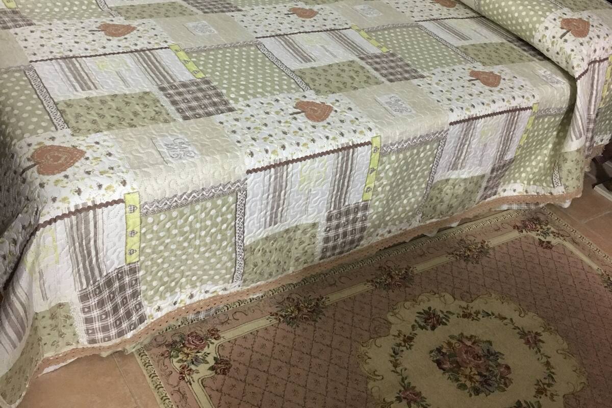 Una cama con cubrecama acolchado y almohada a juego, alfombra estampada y suelo de baldosas.