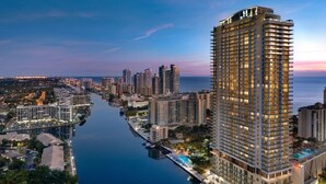 A high-rise hotel with a pool, located near a body of water and other buildings.