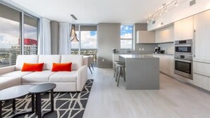 A modern apartment with a living area, kitchen, and large windows offering a city view.