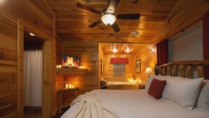A cozy log cabin room with a bed, a ceiling fan, and a fireplace. - Heavenly View – Romantic Pigeon Forge Cabin with Hot Tub, Jacuzzi & Pool Table (Sevierville)