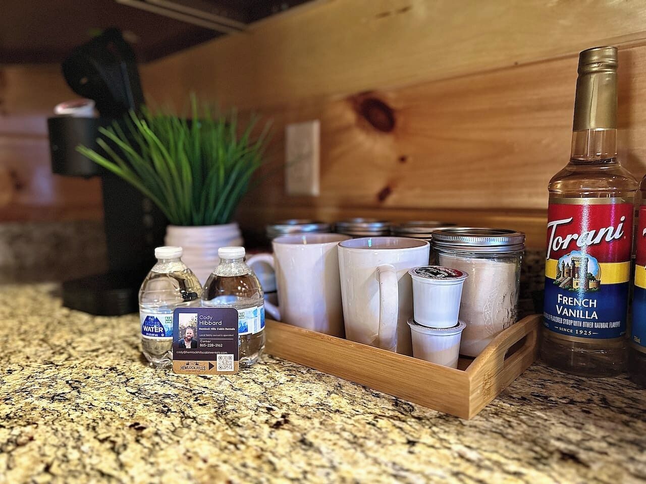 Una encimera de cocina con una botella de agua, un frasco de Torani French Vanilla y varios utensilios y recipientes de cocina.