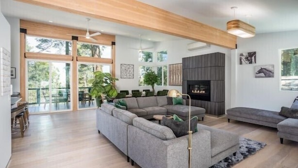 A spacious living room with a sectional sofa, a fireplace, and large windows offering a view of the outdoors. - Scenic Wonders Adventure Lodge 3 Bedroom (Yosemite National Park)