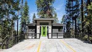 A building with a green door, surrounded by tall trees. - Scenic Wonders Adventure Lodge 3 Bedroom (Yosemite National Park)