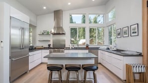 A modern kitchen with a large island, stainless steel appliances, and a view of the outdoors through large windows. - Scenic Wonders Adventure Lodge 3 Bedroom (Yosemite National Park)