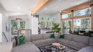 A modern living room with a grey sectional sofa, a coffee table, and a large window offering a view of trees. - Scenic Wonders Adventure Lodge 3 Bedroom (Yosemite National Park)