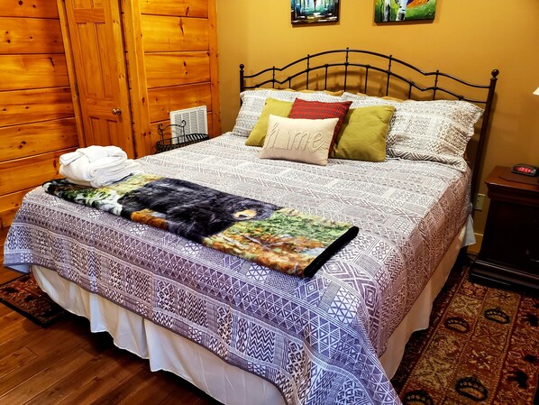 Una cama bien hecha con una colcha estampada y almohadas, un armario de madera y una mesita de noche con un reloj.