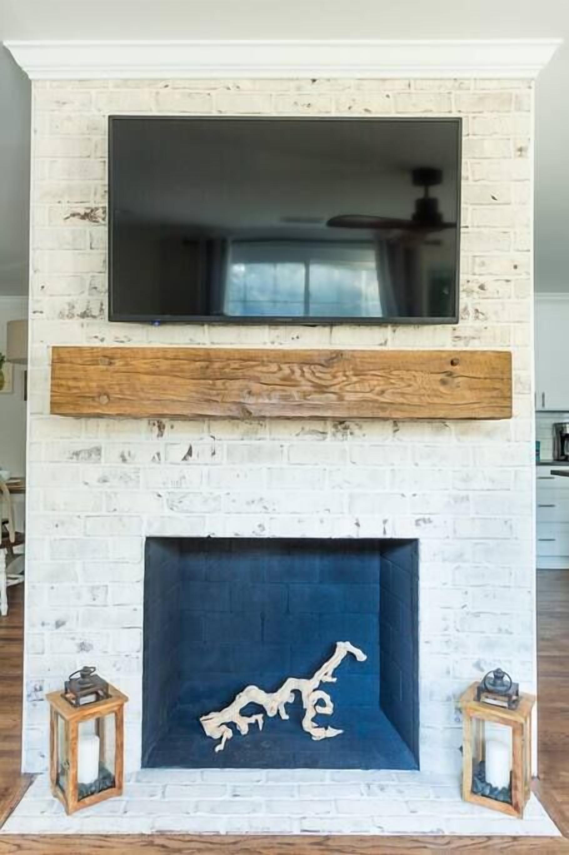 A white brick fireplace with a blue hearth, a wooden mantel, and two lanterns.