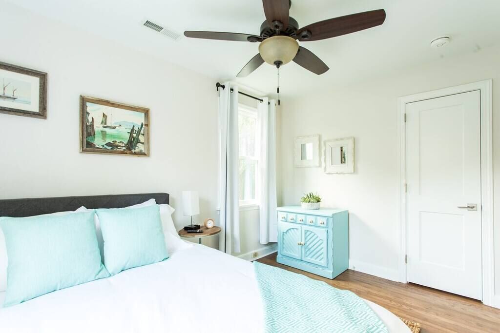 A bedroom with a bed, a ceiling fan, a nightstand, a dresser, and a door.