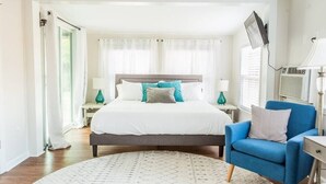 Une chambre à coucher avec un lit, un fauteuil bleu, une télévision et une fenêtre avec des rideaux.