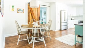 Un coin repas avec une table et des chaises en bois, un luminaire suspendu et une cuisine en arrière-plan.
