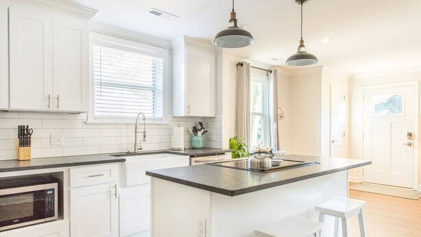 Une cuisine moderne avec des meubles blancs, un îlot central et des luminaires suspendus.