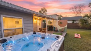 Un jardin avec un jacuzzi, une terrasse avec des chaises et une plateforme en bois.