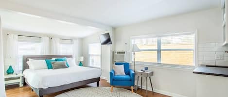 A bedroom with a bed, a blue armchair, a round rug, and a window with blinds.