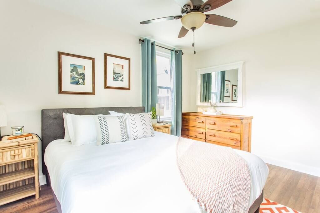Een slaapkamer met een bed, een houten dressoir, een plafondventilator en twee ingelijste foto's aan de muur.