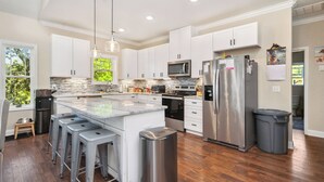 Una cocina moderna con armarios blancos, electrodomésticos de acero inoxidable y una isla central con taburetes de bar.