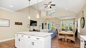 Una cocina amplia con una isla grande, piso de madera, iluminación colgante y ventilador de techo.