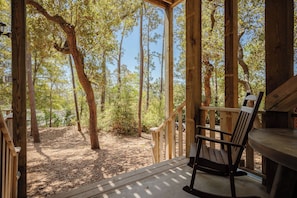 A wooden deck with a chair and table, surrounded by trees and a clear sky. - Tranquil Harbor: Private Pool, Dock and Canal Views (Oak Island)