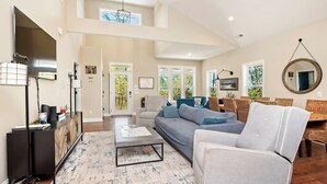 Un amplio salón con sofá, mesa de centro y televisor sobre un mueble. Hay una zona de comedor con mesa y sillas.