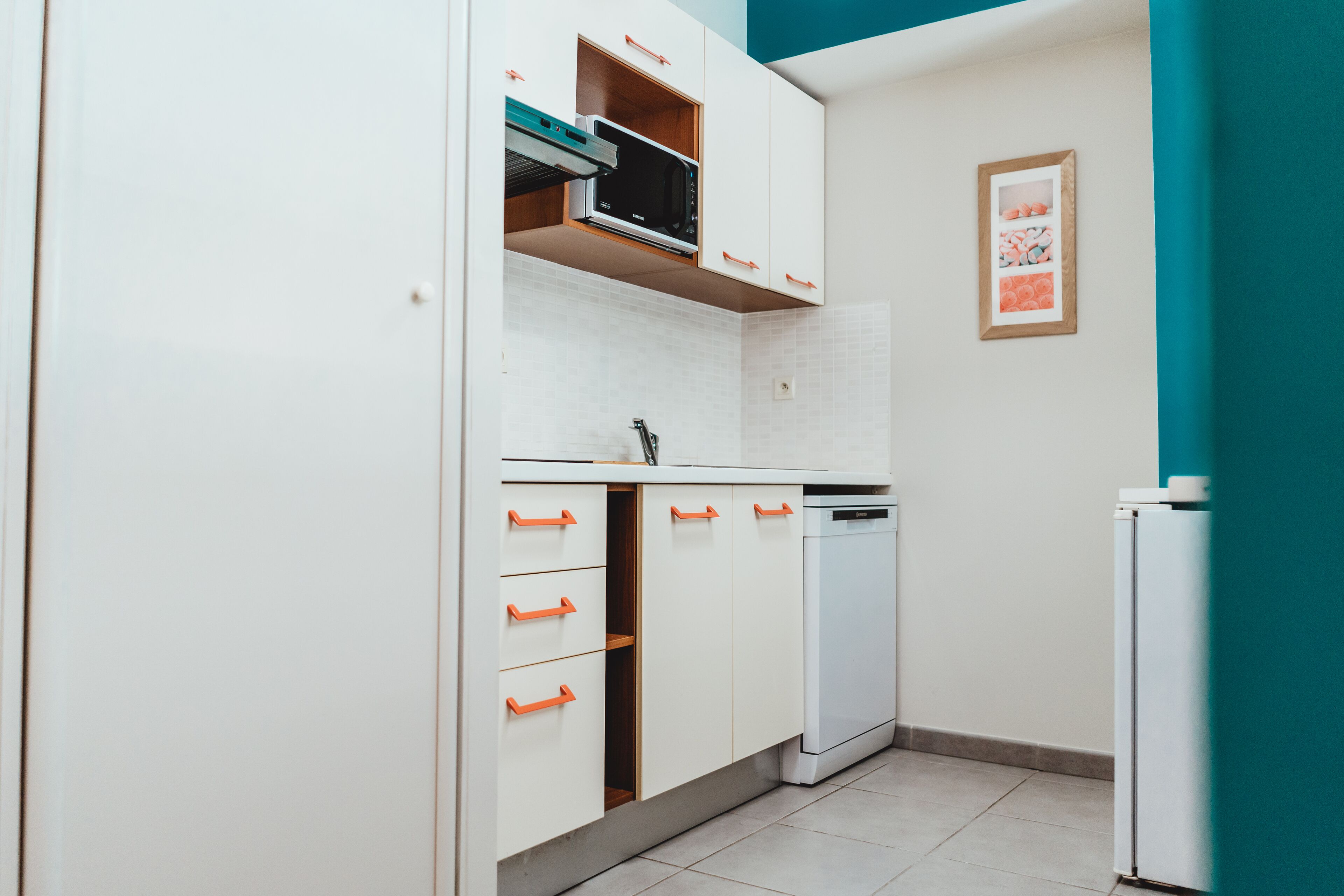 Una cucina compatta con mobili bianchi, un forno a microonde, una lavastoviglie e un frigorifero.