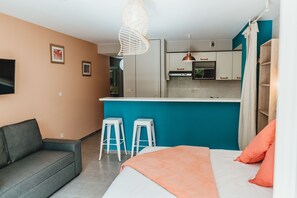 A modern living room with a sofa, a bed with an orange throw, and a kitchen area with a microwave and bar stools. - Magnificent F1 Apartment, The Coral Garden, in the Heart of Saline les Bains (La Saline-Les-Bains)