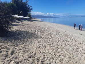 Ein sandiger Strand mit Sonnenschirmen und ruhiger See.
