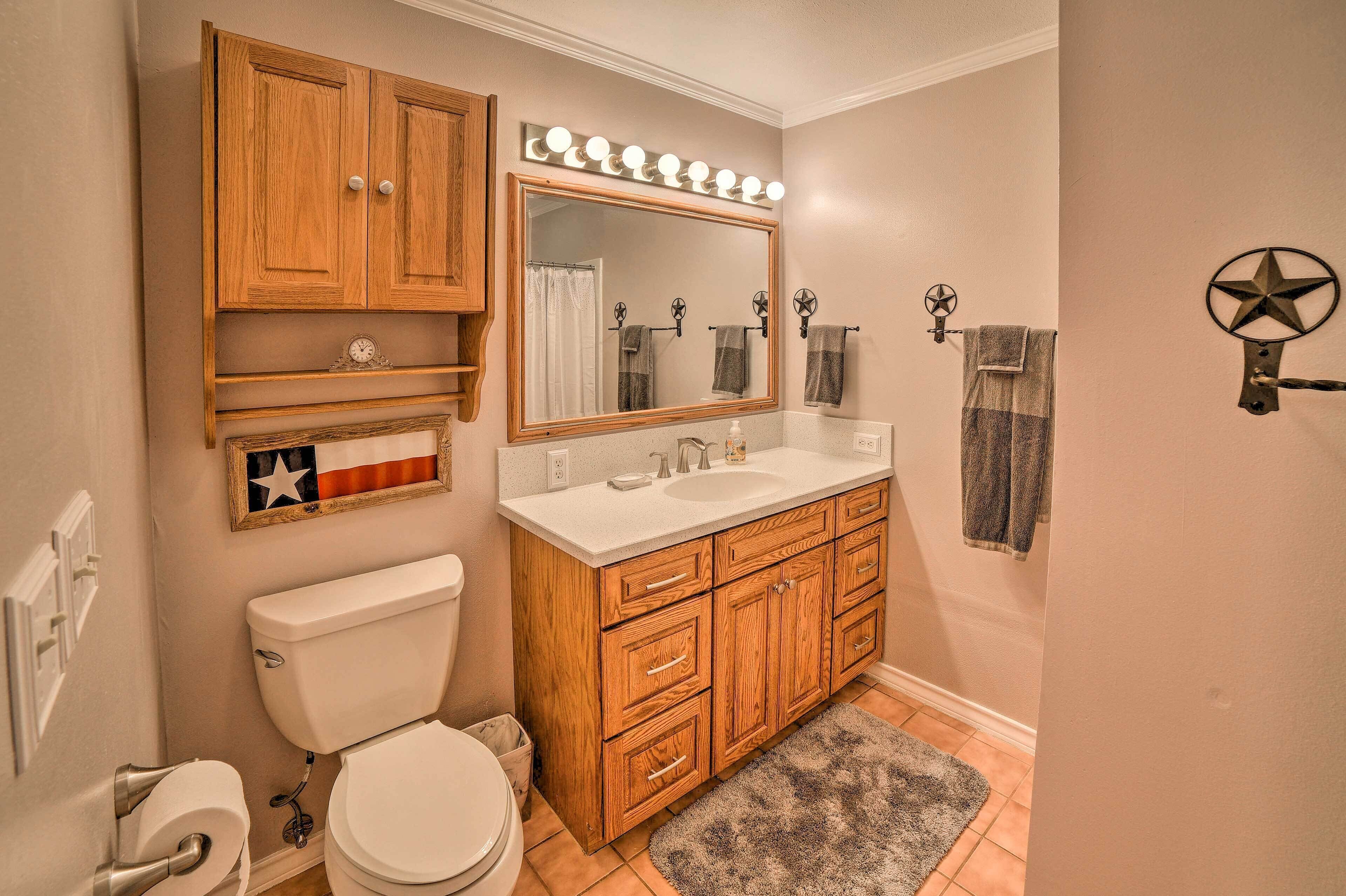 A bathroom with wooden cabinets, a large mirror with lights, a toilet, and a sink.