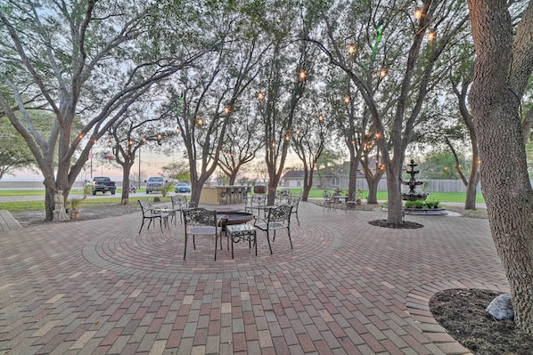 Une terrasse dallée avec un espace salon circulaire, entourée d’arbres et éclairée par des lampes extérieures.