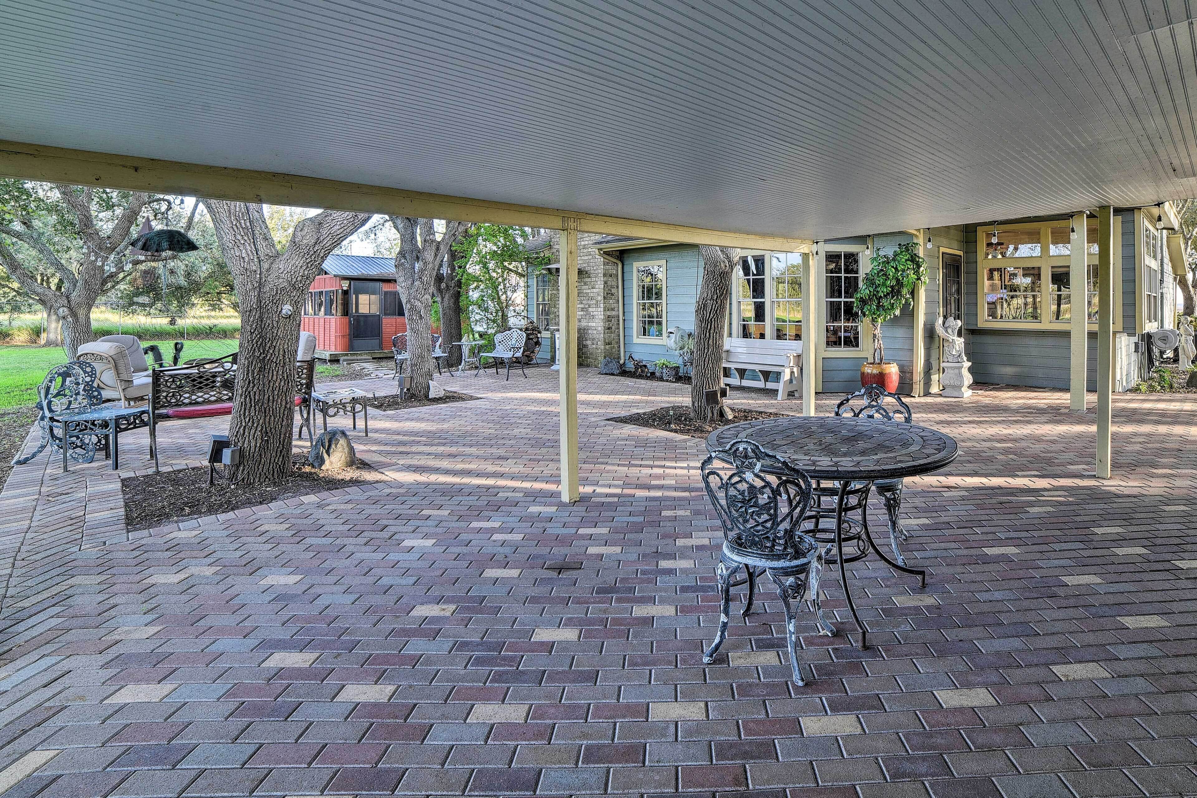 A covered patio with brick flooring, outdoor furniture, and a view of a house in the background.