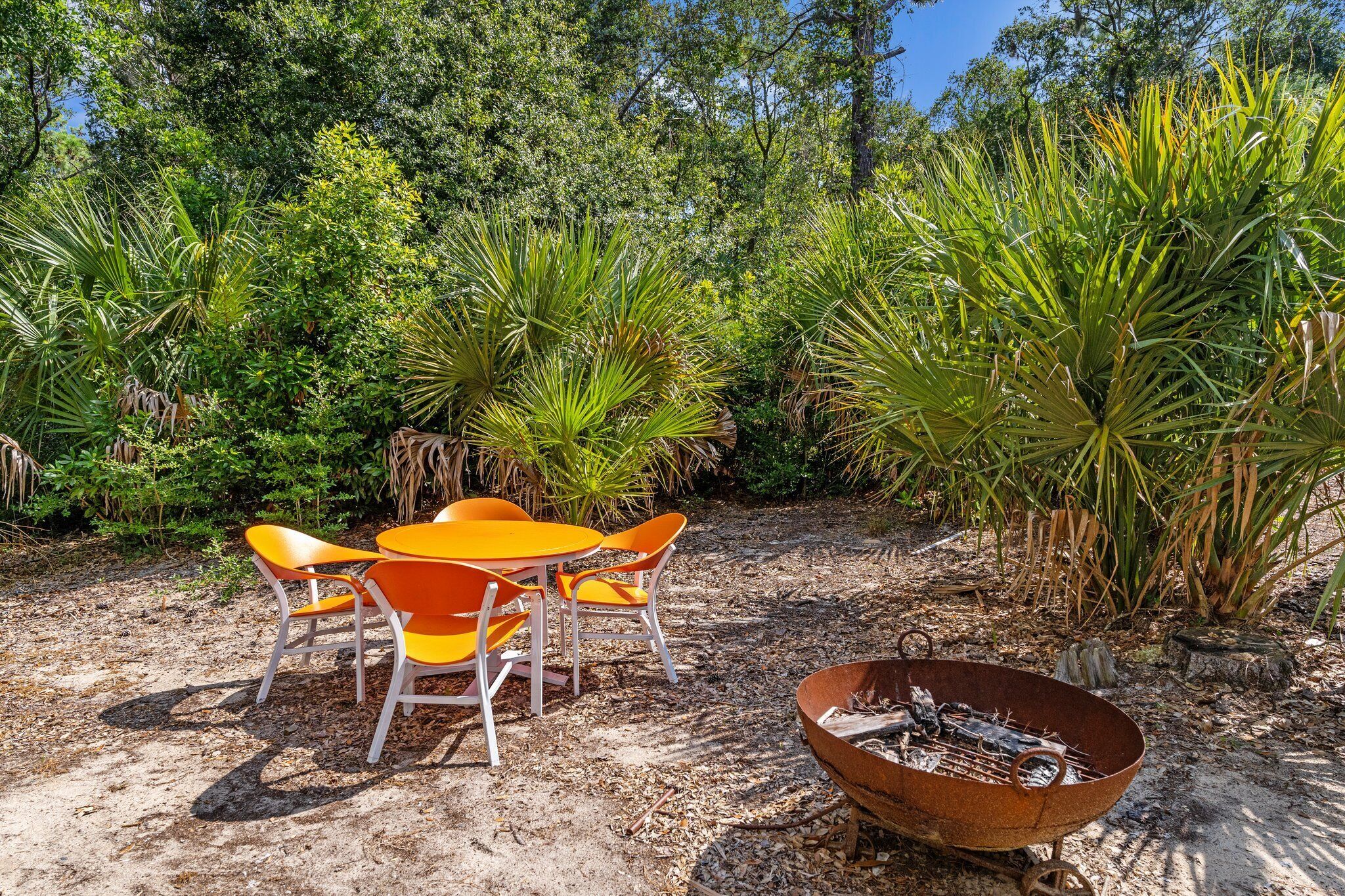 An outdoor seating area with a fire pit, surrounded by lush greenery and trees.