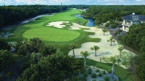 Un parcours de golf doté d’obstacles d’eau, de bunkers de sable et d’une grande maison avec un balcon.