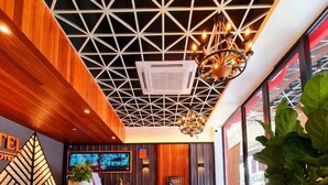 Zona de recepción de un hotel con suelo de diseño geométrico, un mostrador de madera, una lámpara moderna y una planta grande en maceta.