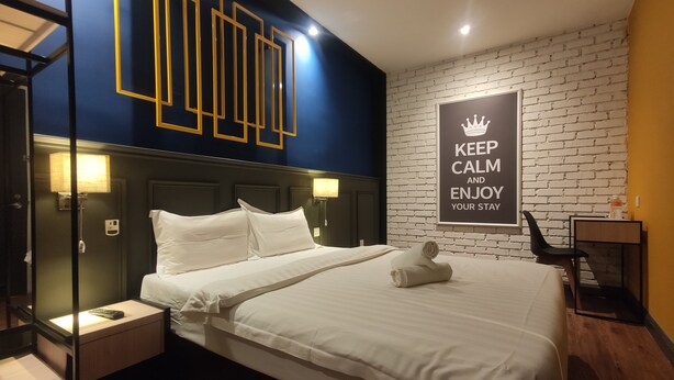 Una habitación de hotel con cama, mesitas de noche, un cartel motivacional en la pared y una pared con diseño de ladrillos.