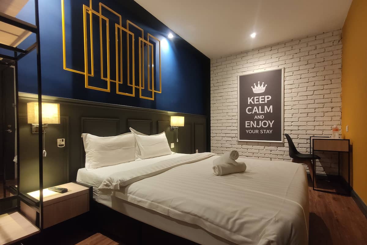 A hotel room with a bed, bedside tables, a wall with a motivational poster, and a brick-patterned wall.