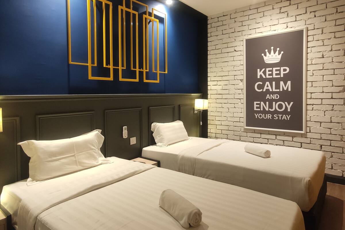 A hotel room with two beds, a dark blue accent wall, a white brick accent wall, and a motivational sign.