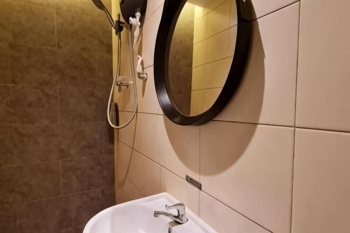 Baño con lavamanos blanco, espejo redondo y ducha.