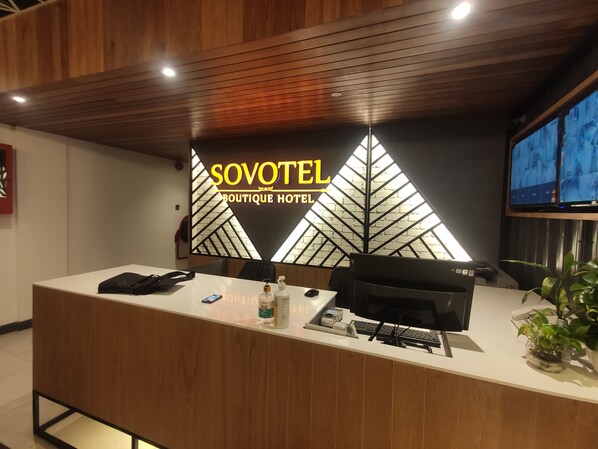 Een receptiebalie bij SOVOTEL Boutique Hotel met een modern design, een computer, een telefoon en een plant.