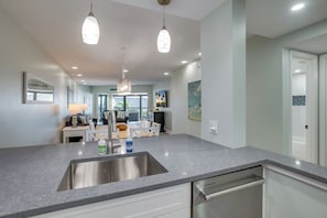 A modern kitchen with a stainless steel sink, pendant lighting, and a view to the living area.