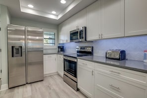 A modern kitchen with stainless steel appliances, white cabinetry, and a herringbone-patterned backsplash.