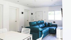 Un salon moderne avec un canapé en cuir turquoise, une table à manger blanche et une petite table d’appoint blanche.