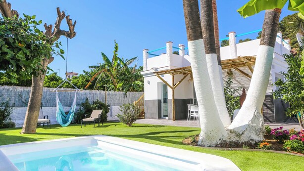 Un jardin avec une piscine, un hamac et une maison blanche dotée d’un patio abrité.