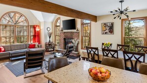 A spacious living room with a fireplace, a large TV mounted above it, and a dining area with a table and chairs. - Cozy Creekfront House with Sauna (Bushkill)