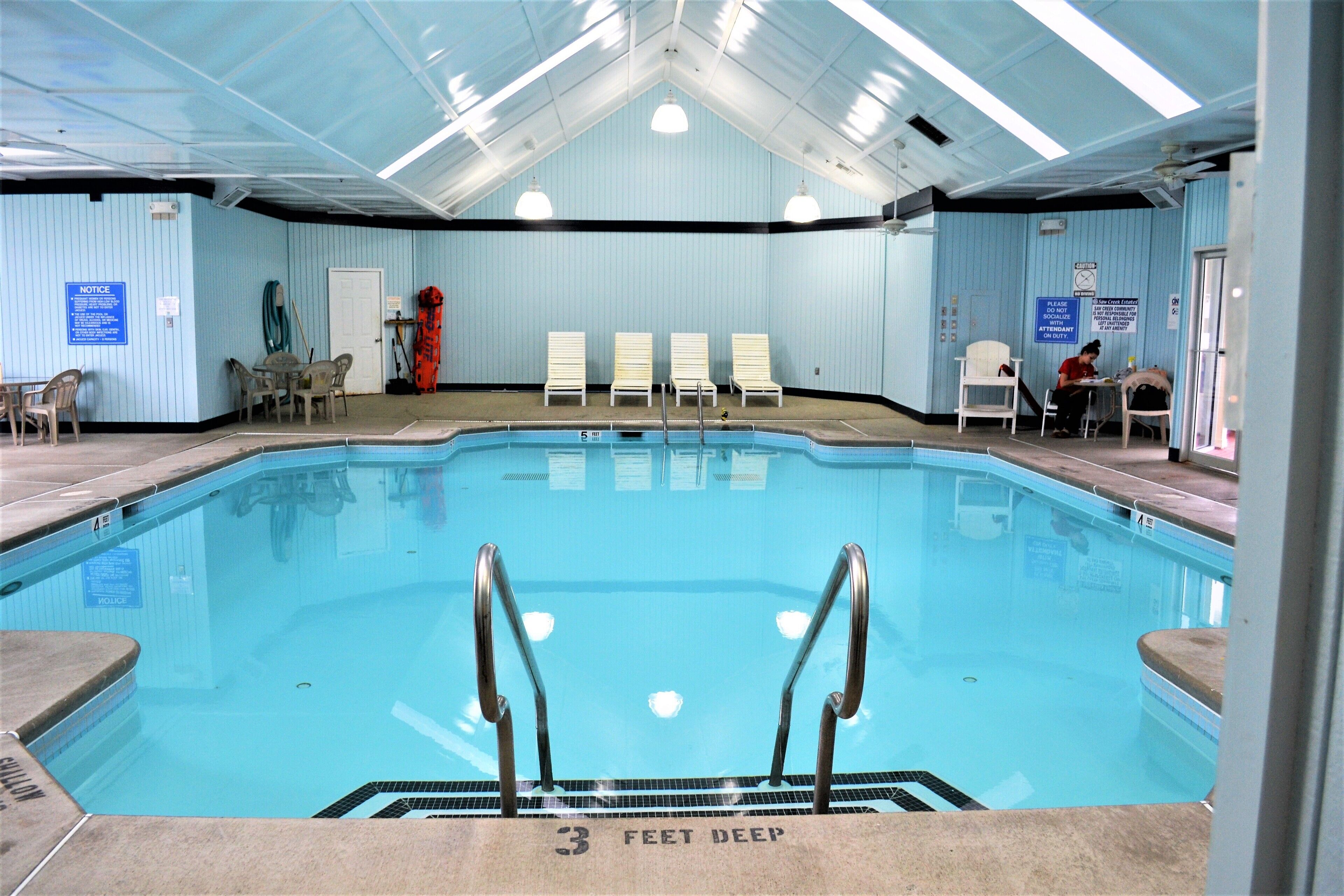 An indoor swimming pool with clear water, a 3 feet deep sign, and several lounge chairs.