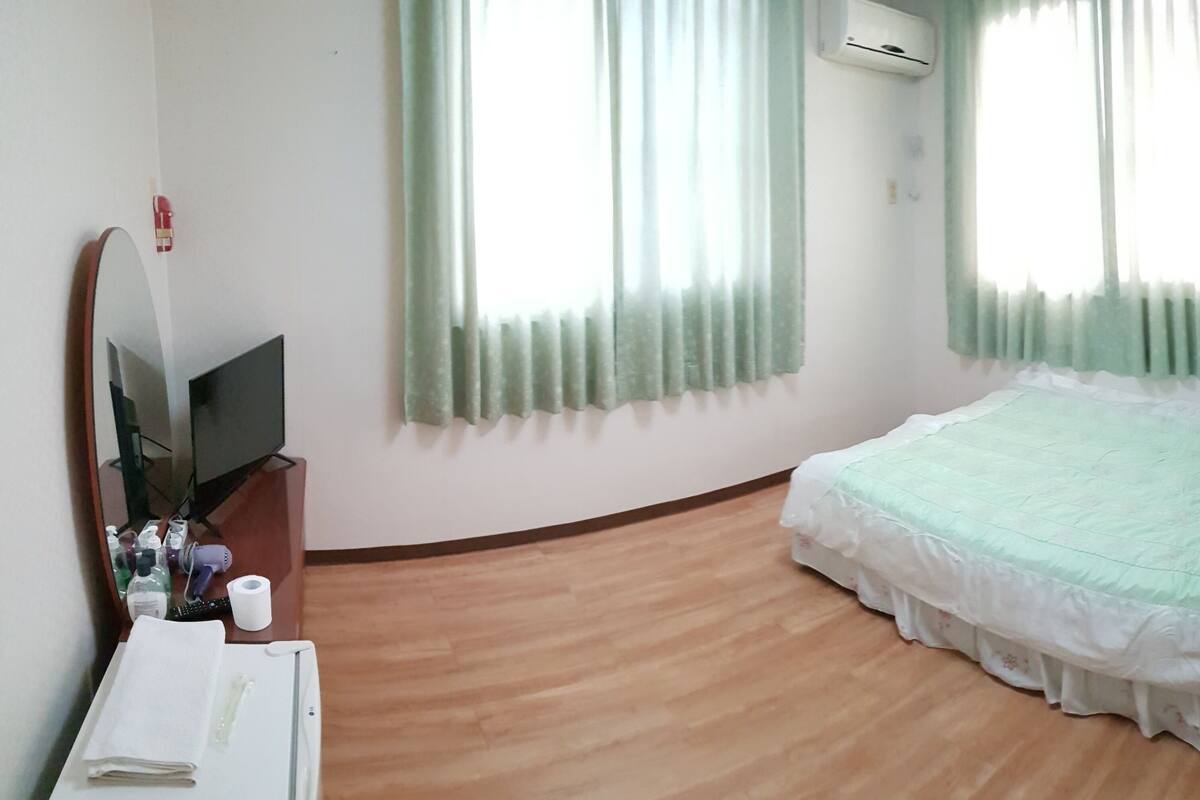 Ein Hotelzimmer mit Bett, Fernseher, Spiegel und Holzboden.